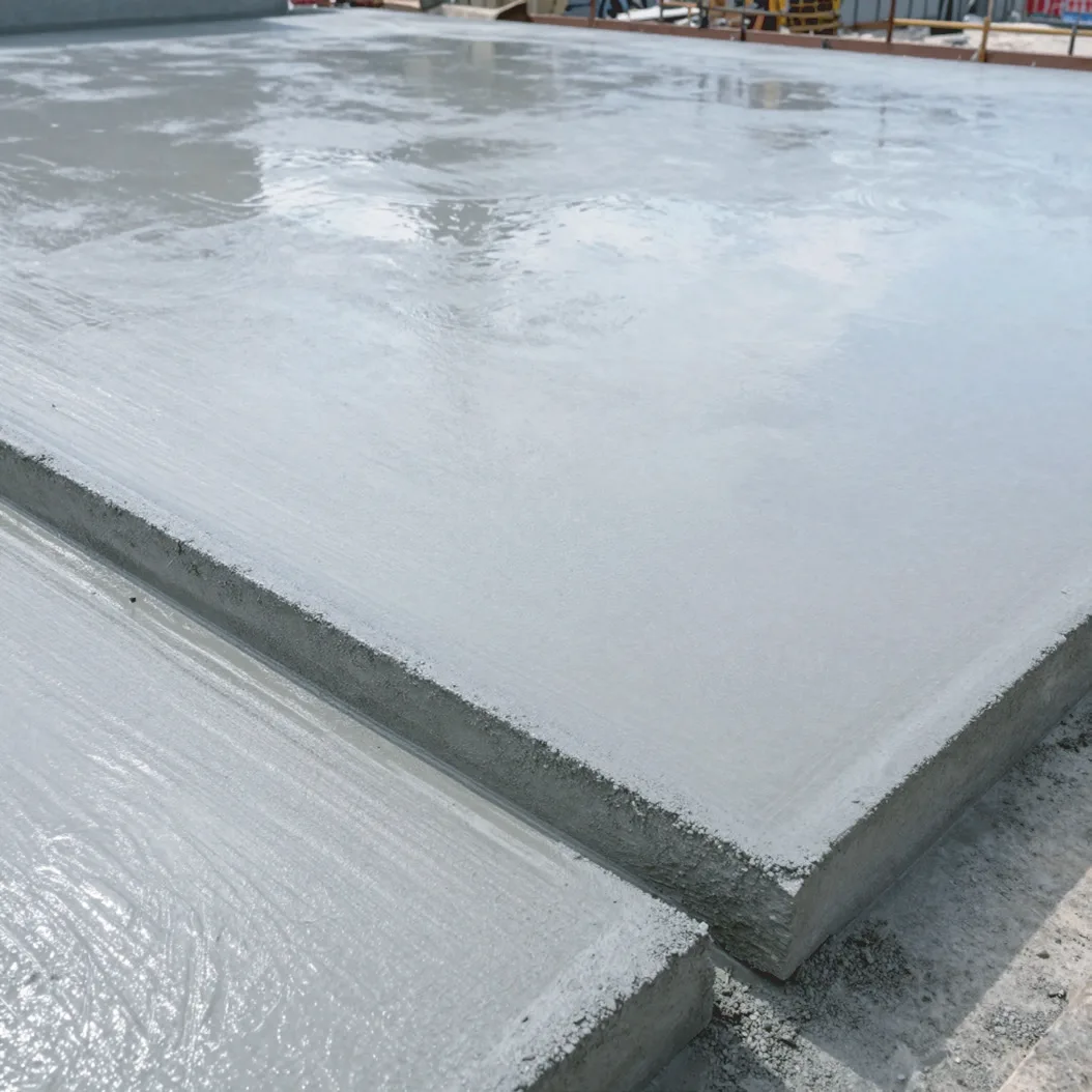 Close view of the edge of a newly placed concrete slab, its finished surface still wet, with plastic sheeting covering the bay next to it