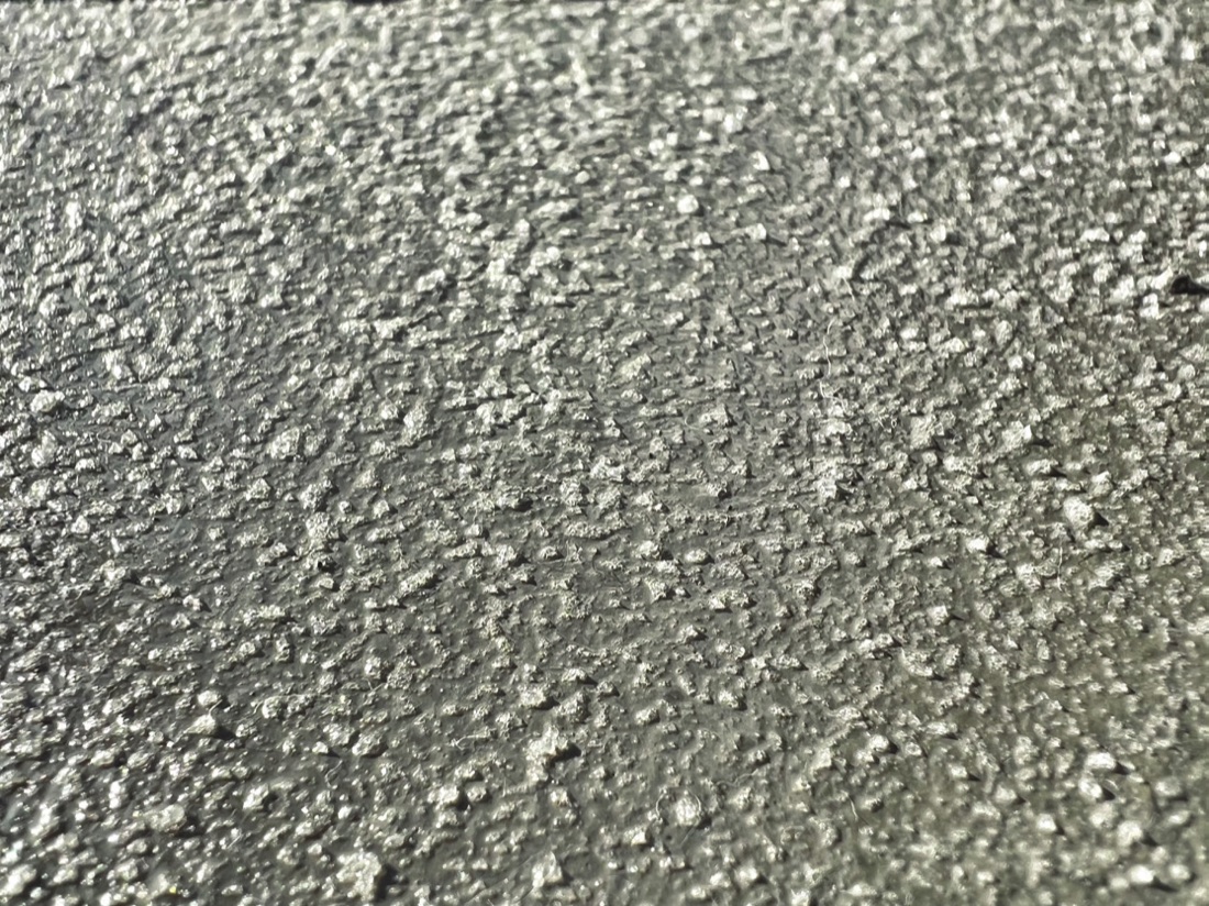 Close-up photograph of a gray coated concrete surface showing a fine, granular, lightly speckled texture catching the light