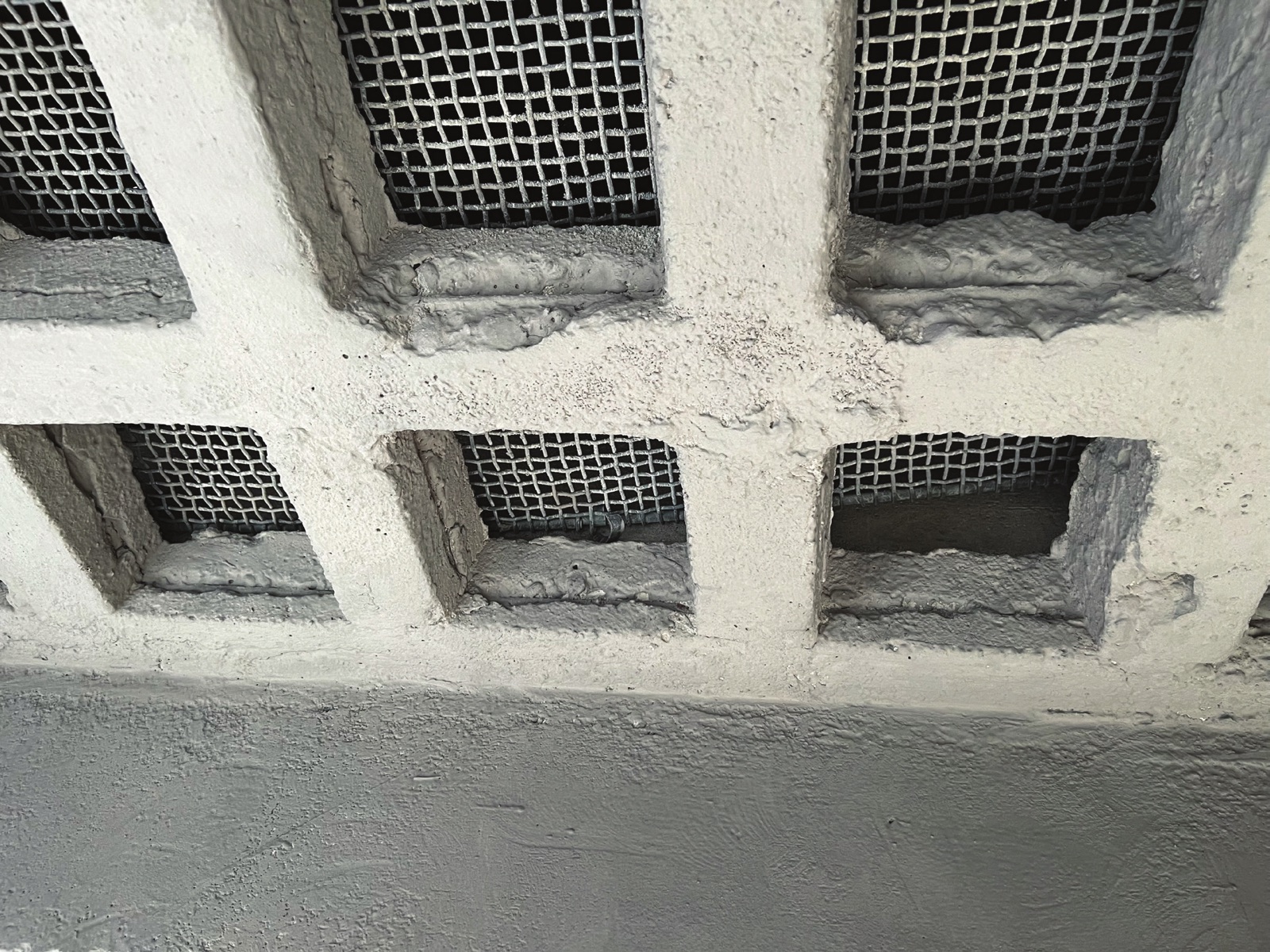 Close view of a row of vent openings in a treated concrete reservoir wall, each opening fitted with a wire mesh screen