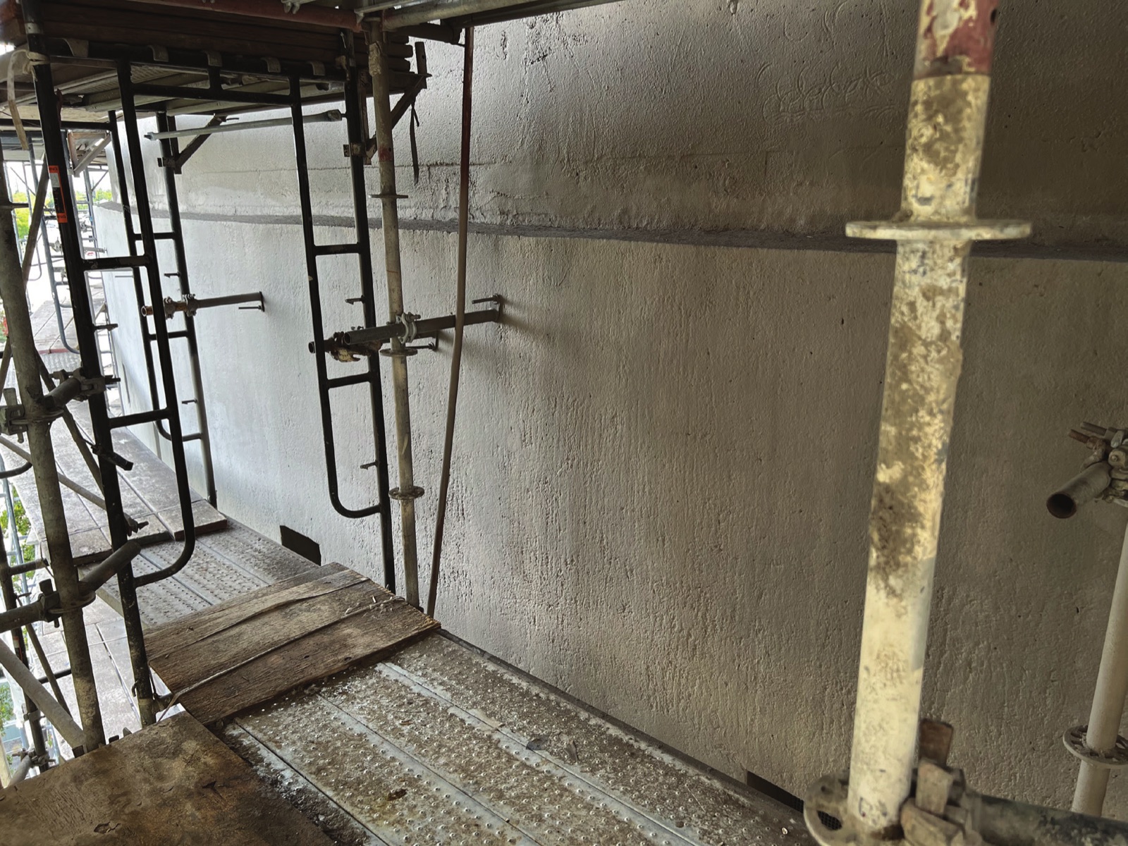 Scaffolding erected tight against a curved concrete reservoir wall, with the wall face pale and freshly treated above and below a horizontal construction joint