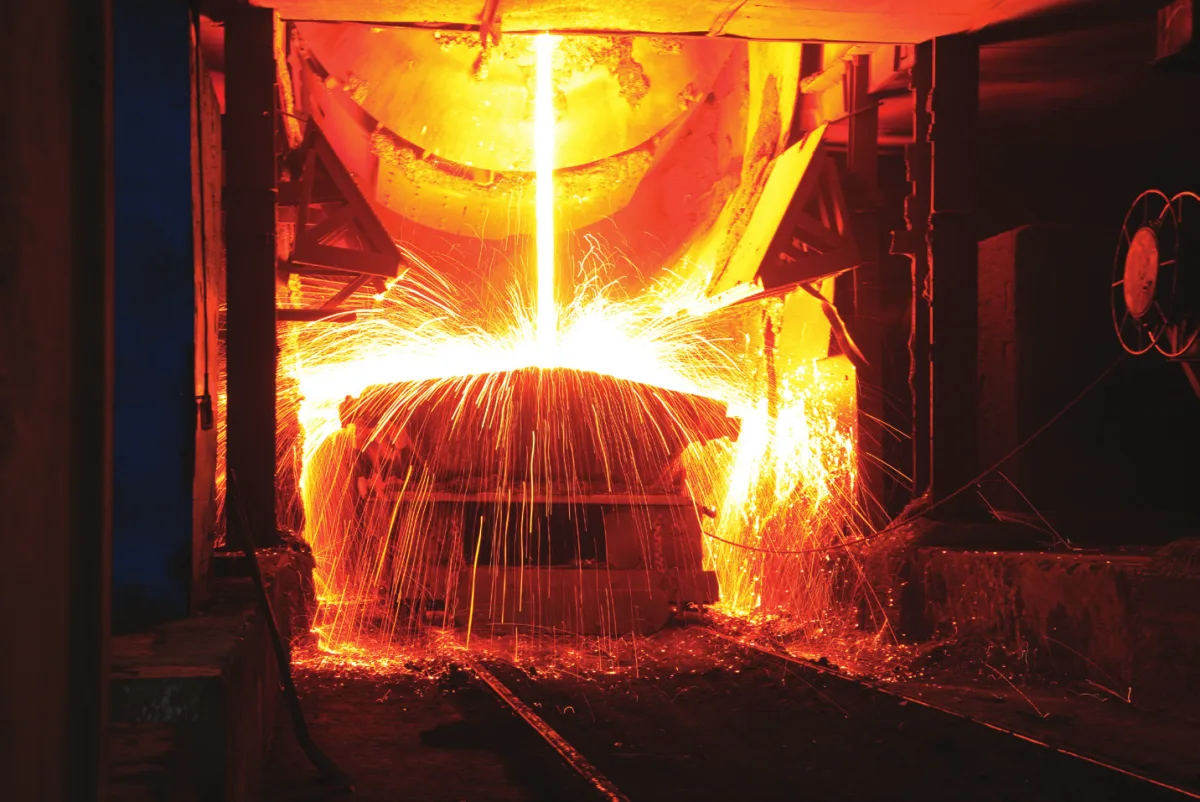 Molten metal pouring from a ladle inside a foundry, throwing sparks across the floor