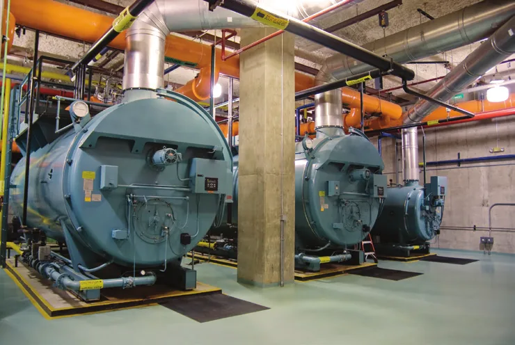 Two large boilers standing on concrete plinths in a plant room beside a concrete column
