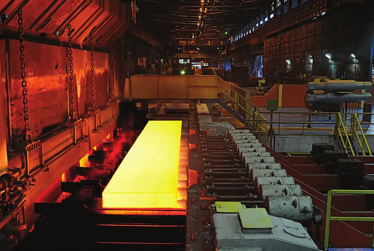 Glowing hot steel slab travelling along a roller line in a steel mill