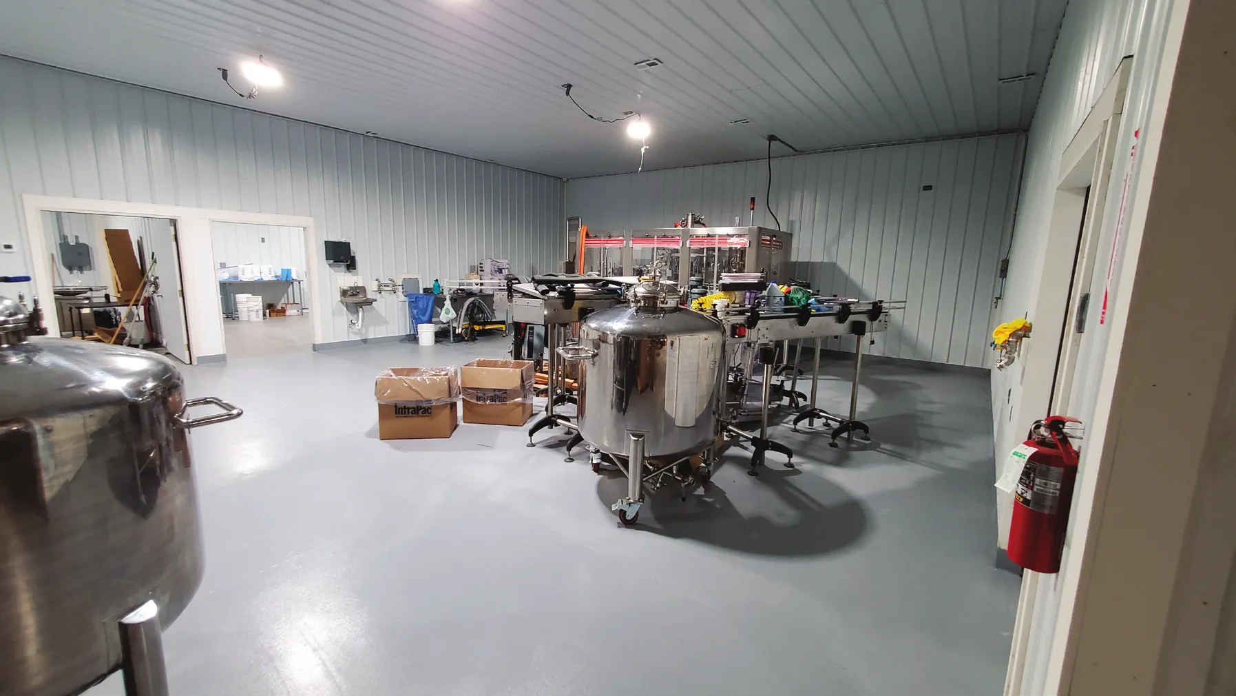 Beverage production room with a seamless gray floor, stainless steel tanks and a bottling line in place